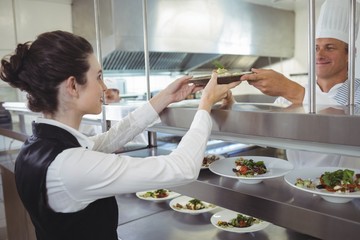 Chef handing food dish to waitress at order station