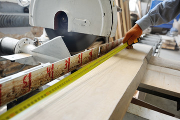 Carpenter makes the marking of the board with a measuring tape measure on the background of the joiner's workshop