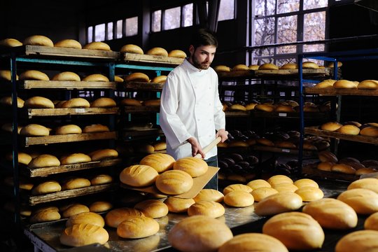 young handsome guy baker pulls out of the oven fresh bread at the bakery background
