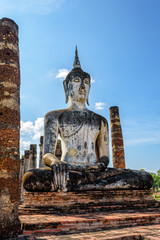Obraz premium Ancient Buddha statue sitting among the ruins under the bright sky of Wat Maha That temple in Sukhothai Historical Park is an old city and famous tourist attraction of Sukhothai Province, Thailand