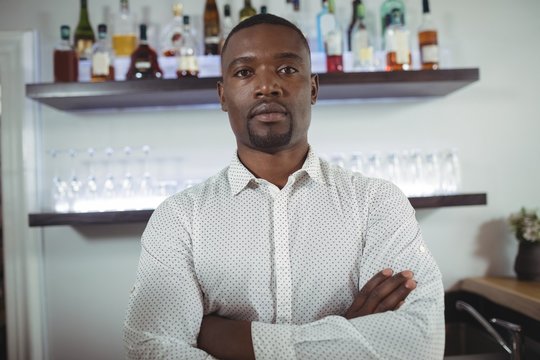 Portrait of bar tender standing with arms crossed at bar counter