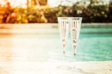 Two glasses of prosecco  cocktail with blueberries at the edge of a resort pool. Concept of luxury vacation - obrazy, fototapety, plakaty
