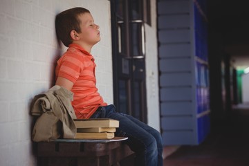 Sad boy with eyes closed sitting on bench by wall in corridor