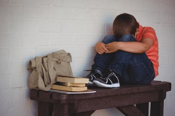 Full length of unhappy boy sitting on bench by wall