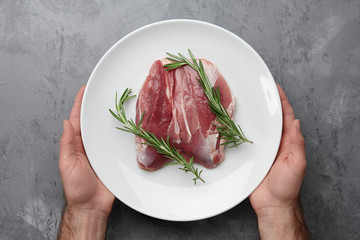 Man's hands holding a big white plate with raw duck breast on gray stone background