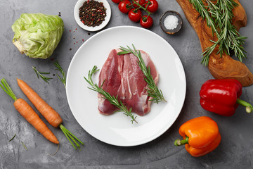 Raw duck breast, fresh vegetables, herbs and spices on gray stone background, top view