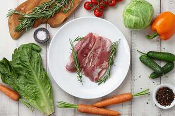 Raw duck breast in plate and fresh vegetables on white wooden background