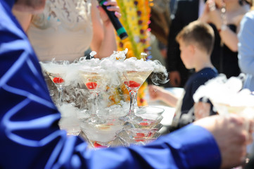 A slide of champagne with dry ice and smoke at the solemn event. Pyramid of glasses with alcohol and cherries.