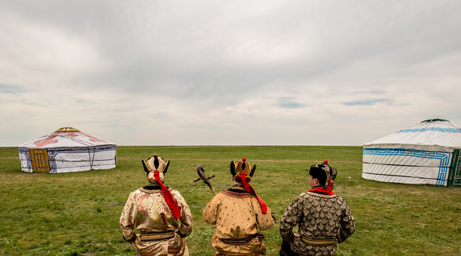 Three Kalmyk musicians in national costumes in the steppe against the background of yurts, the spring steppe