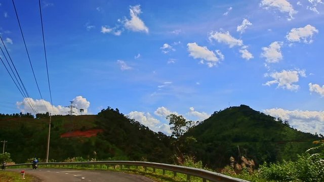 Camera Follows Scooter along Country Road among Hilly Landscape