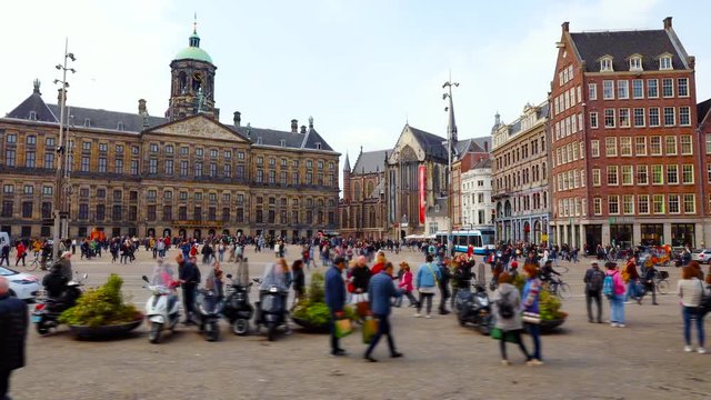 Central square of Amsterdam city in Netherlands time-lapse video. Crowds of people tourists walking amon famous landmarks buildings. Sunny day. Local public transport, trams and buses.