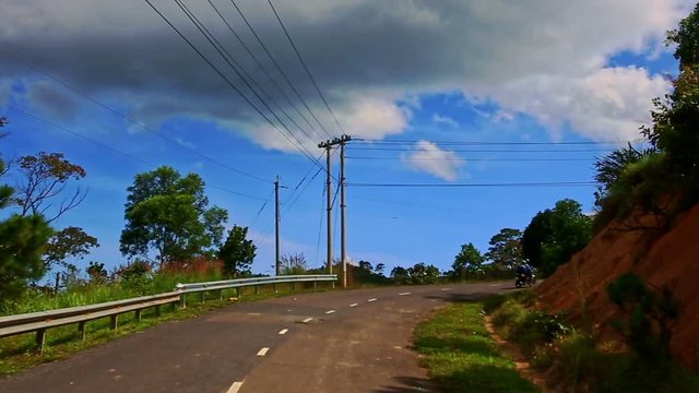 Camera Follows Scooter along Country Road among Hilly Landscape