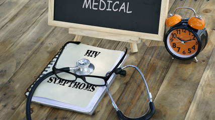 notebook with the words "HIV SYMPTHOMS" and stethoscope, glasses, chalk board, alarm clock on a wooden table. medical and healthcare concept.