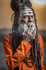 Portrait of sadhu smoking and standing with sunrise behind him, Varanasi, India.