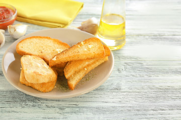 Plate with tasty garlic French bread slices on wooden table