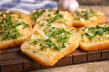 Tasty bread slices with garlic, cheese and herbs on wooden cutting board