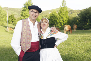 Couple dressed with one of the traditional Basque Country dresses, outdoors, smiling on the meadow.