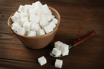 Bowl with sugar cubes and spoon on wooden table