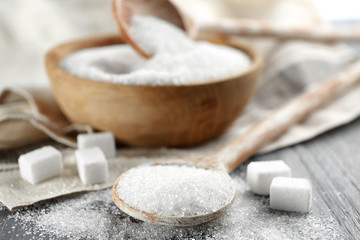 Wooden spoon and bowl with sugar on table, closeup