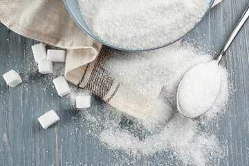 Bowl and spoon with sugar on wooden background