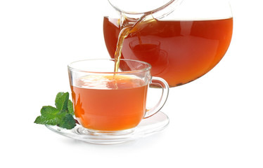 Pouring black tea into glass cup from teapot on white background