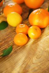 Appetizing fresh citrus fruits with green leaves on wooden background