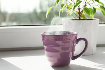 Cup of delicious hot drink on window sill