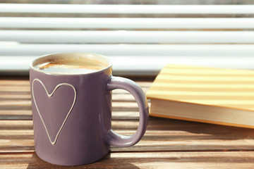 Cup with delicious coffee and book on window sill
