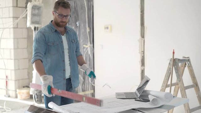 Male architect with blueprints checking wall with level at new home 

