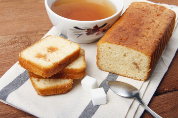 Black tea with sugar and cake with jam on a napkin and on a wooden background