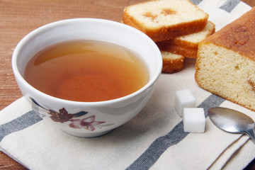 Black tea with sugar and cake with jam on a napkin and on a wooden background
