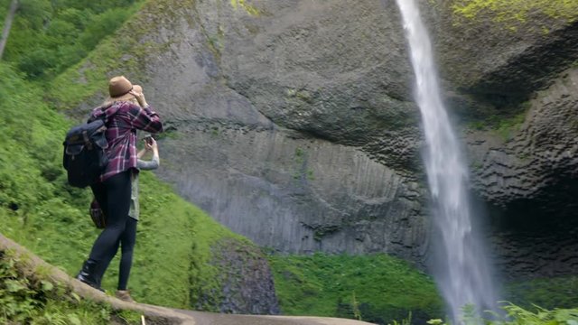 Excited Hikers Reach The End Of The Trail And Take Photos Of Waterfall And Raise Their Arms In Air