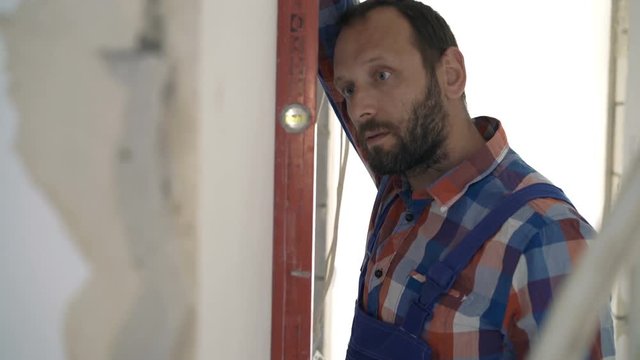 Male worker checking wall with level at new home 
