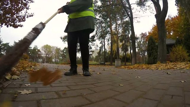 Woman janitor cleaning park from leaves in autumn, most hard and low-paid job