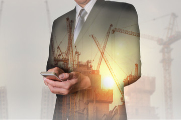 Fototapeta na wymiar Double exposure of businessman hand hold smartphone, mobile, construction crane, building and sunlight of sunset as business, technology, communication and industry concept.