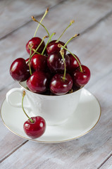 Cherry in a white cup on a light wooden background vertically