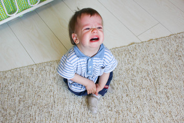 Little boy sitting on the floor, he's upset and crying. The child is crying sitting on the floor in the room..