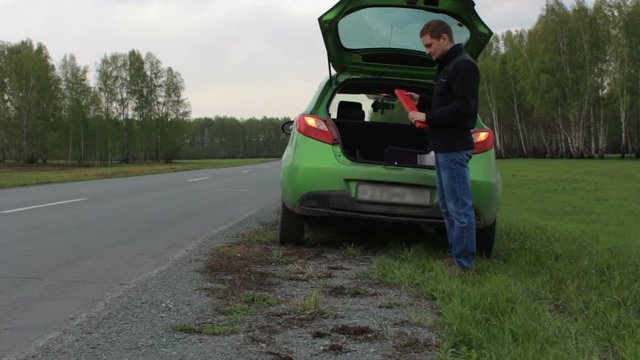 Young man with broken car on the rural road opens trunk