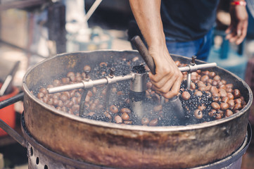 Obraz premium Roasting chestnuts with traditional machinery in a vendor in Chinatown, Malaysia