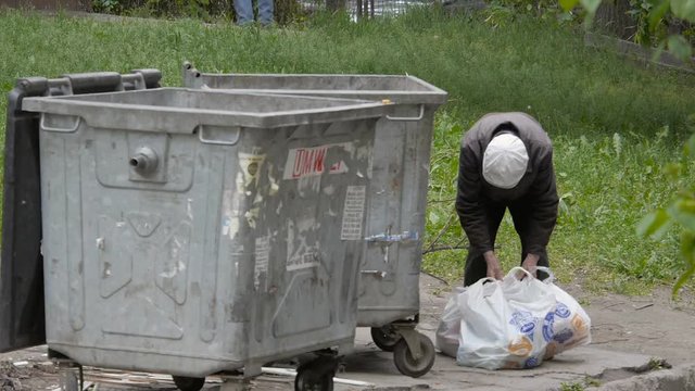 Homeless, infirm and old man puts a waste in packages that has found in garbage cans
