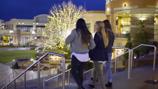 Cute Group Of Teen Friends Laugh Walk Arm in Arm Past Camera And Down A Flight Of Stairs At An Outdoor Shopping Center