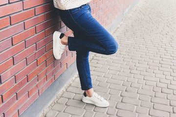 Girl is standing near the wall in jeans and white sneakers