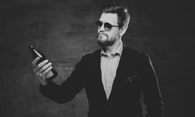 A man dressed in a cotton velvet jacket and sunglasses holds craft bottled beer.