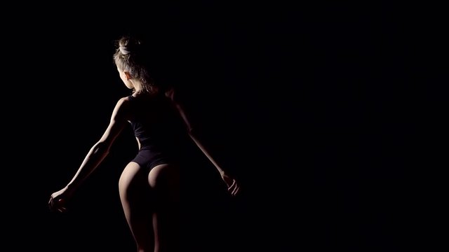 The sexy silhouette of the female body in motion. Sports uploaded pop and spin. Black room interesting light
