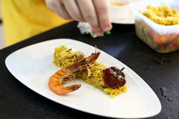 hands preparing a fried rice with olive and prawn on a white plate