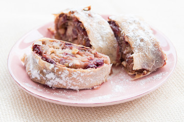 Apple strudel with icing sugar, cherries and raisins on rosa plate