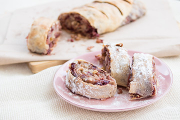 Apple strudel with icing sugar, cherries and raisins on rosa plate