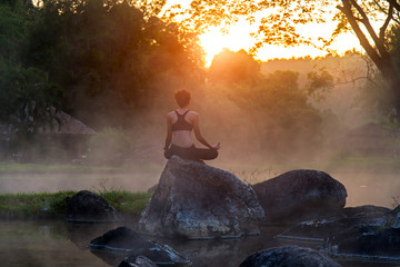 Silhouette of a beautiful Yoga woman in the morning at the hot spring park