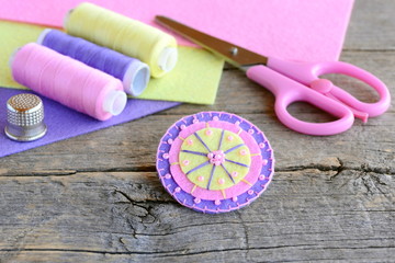Obraz premium Felt round flower decorated with beads. Handmade cute round felt flower, scissors, thread, colored felt sheets, thimble on vintage wooden background. Simple and quick kids sewing project
