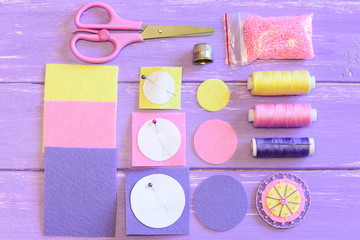 Naklejka premium Cute flower made of felt and beads, colored felt circles and sheets, scissors, paper templates, thread spools, needle, pink beads on a wooden table. Sewing instruction. Teach children to sew. Top view